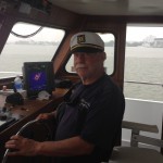 Older man wearing captain hat and steering Judith M fishing boat