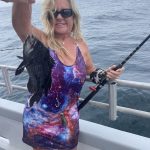 Picture of lady holding sea bass and fishing rod.